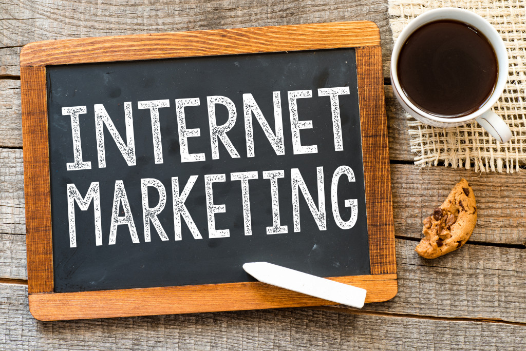 Internet marketing handwritten with white chalk on a blackboard, cup of coffee and biscuit on a wooden background