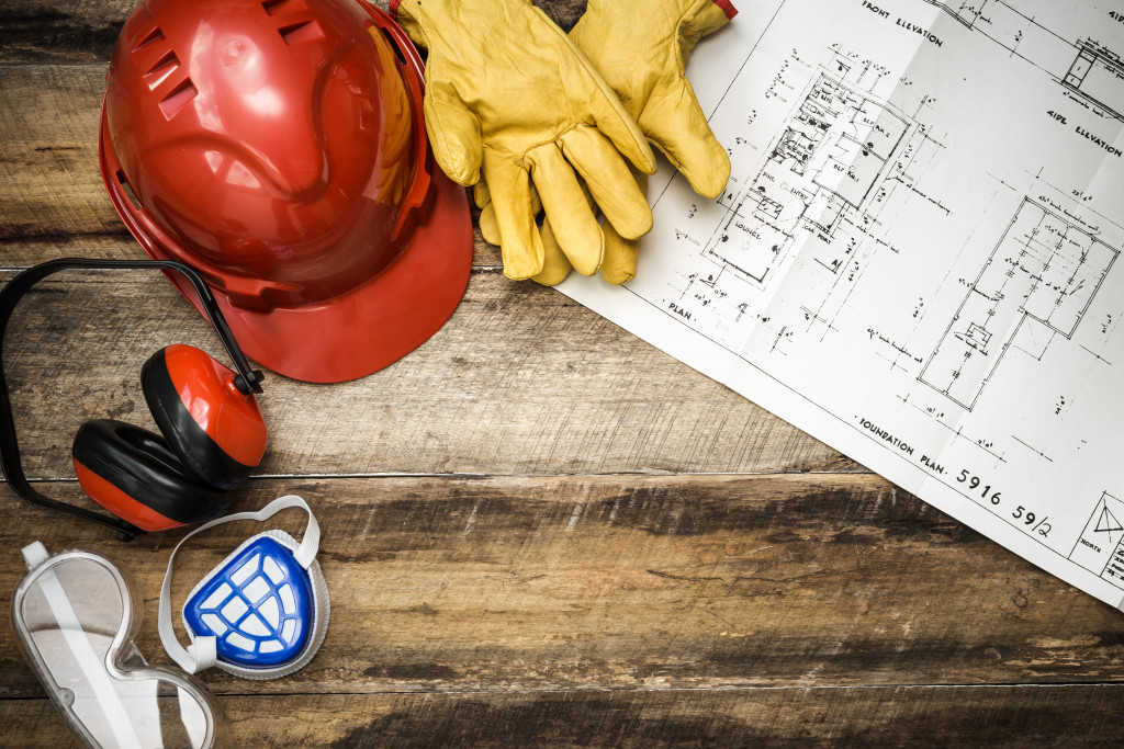 Hardhat, googles, ear protection, and gloves and a blueprint on a table.