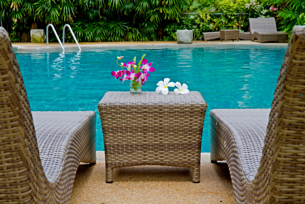 Flowers on a rattan table and some chairs on a poolside 