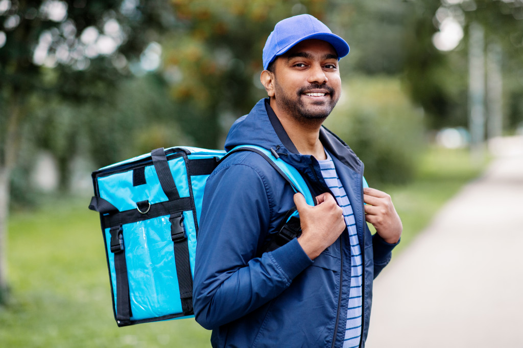 happy smiling indian delivery man with thermal insulated bag on city street