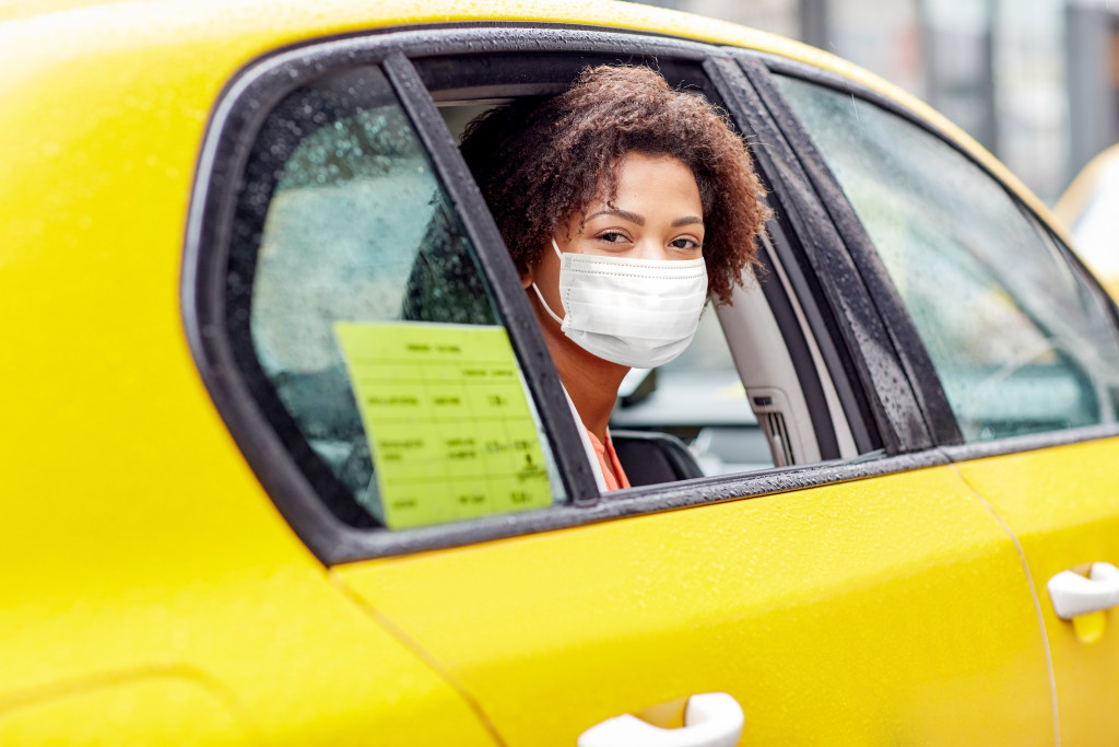 young smiling african american woman in face protective mask driving in taxi on city street