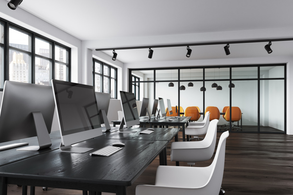 Computers on a table with ergonomic chairs inside a large office.