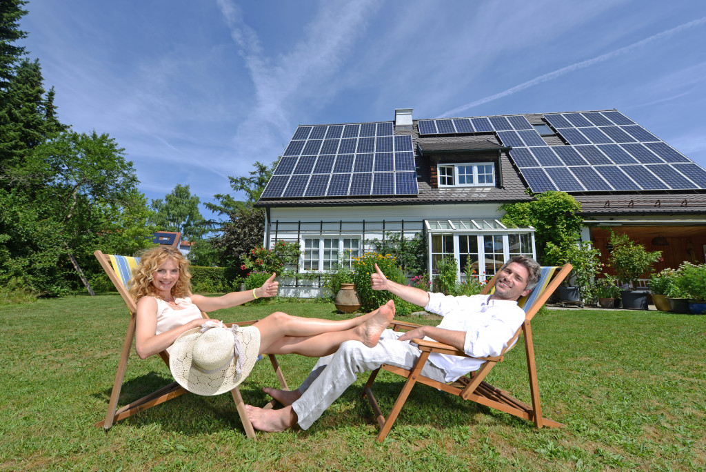 a couple doing an okay sign in front of their solar-paneled house