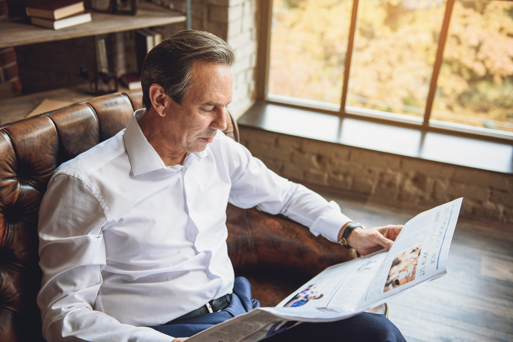 a male businessman reading a newspaper while sitting on a sofa