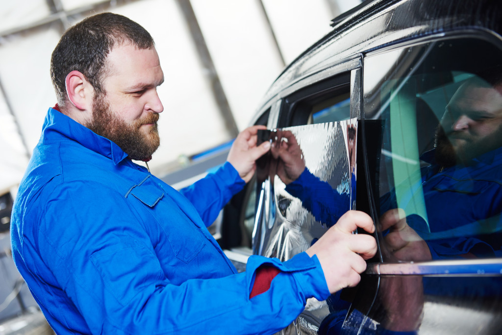 male auto repair mechanic putting tinting to the window of black car