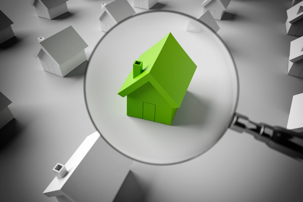 green miniature house under a magnifying glass in a group of random black and white houses