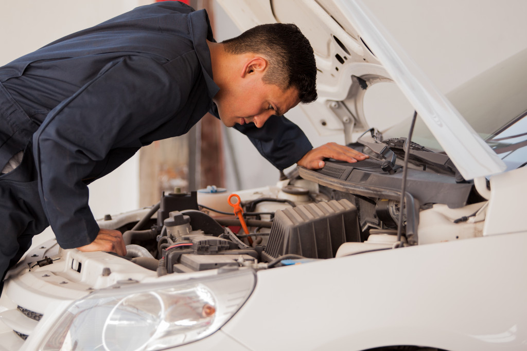 male mechanic in blue overalls checking the engine of a white car