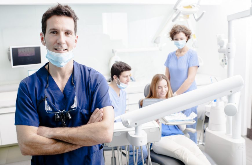 male dentist in the foreground with other assistants and patient at the background