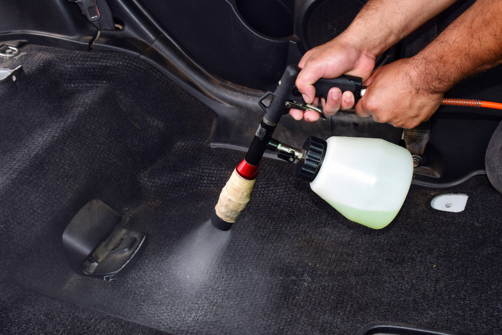 man using sprayer for disinfecting the car's carpet and interior